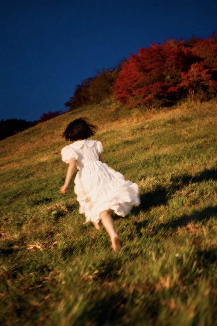 Girl in a white dress running up a grassy hill