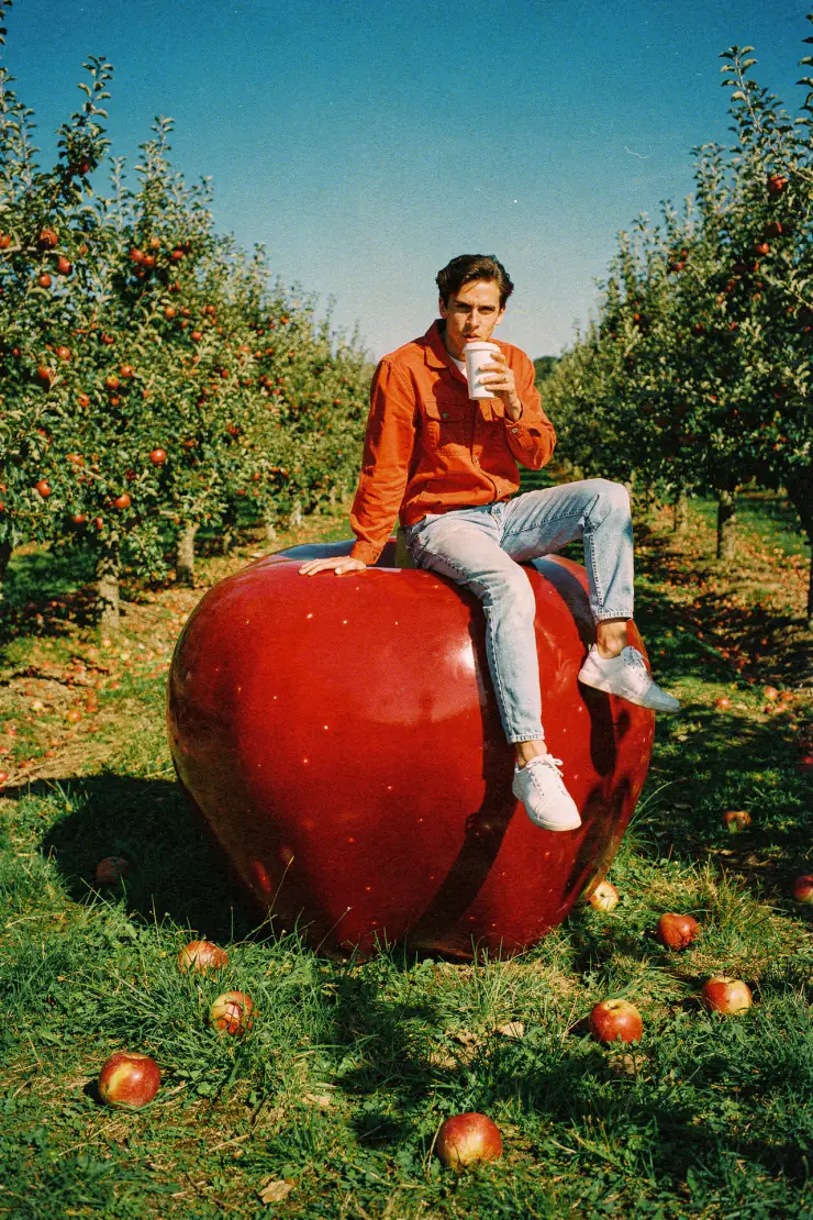Man drinking coffee on a giant red apple in an orchard