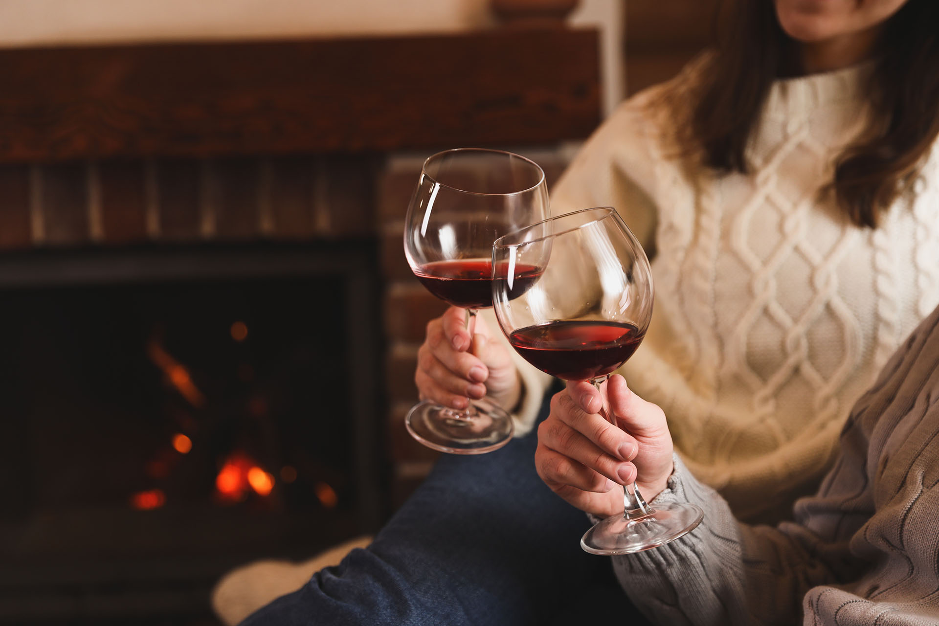 Couple enjoying red wine by fireplace in cosy winter setting.