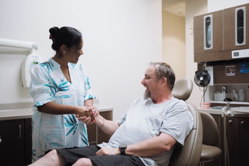 Dentist in teal scrubs consulting with male patient in dental chair, discussing treatment