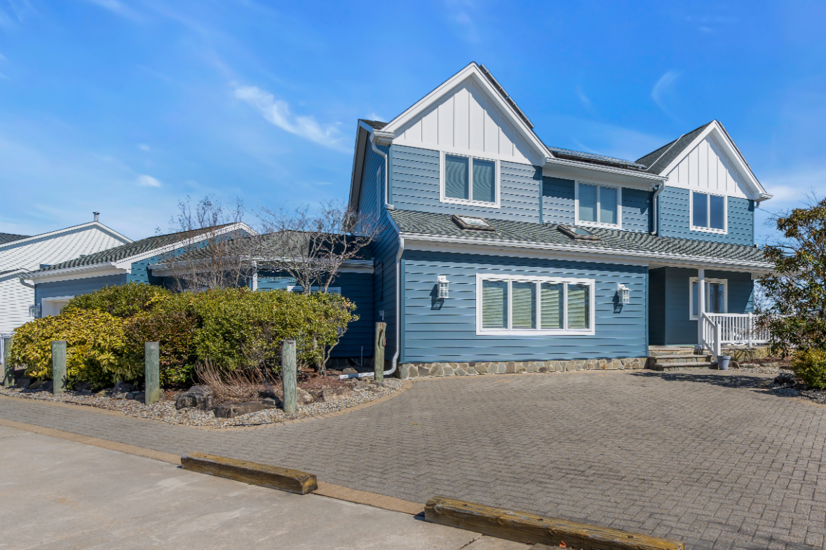 Angled view of beautifully renovated exterior with coastal blue siding and a brick driveway on Allen Rd in Bayville, NJ.