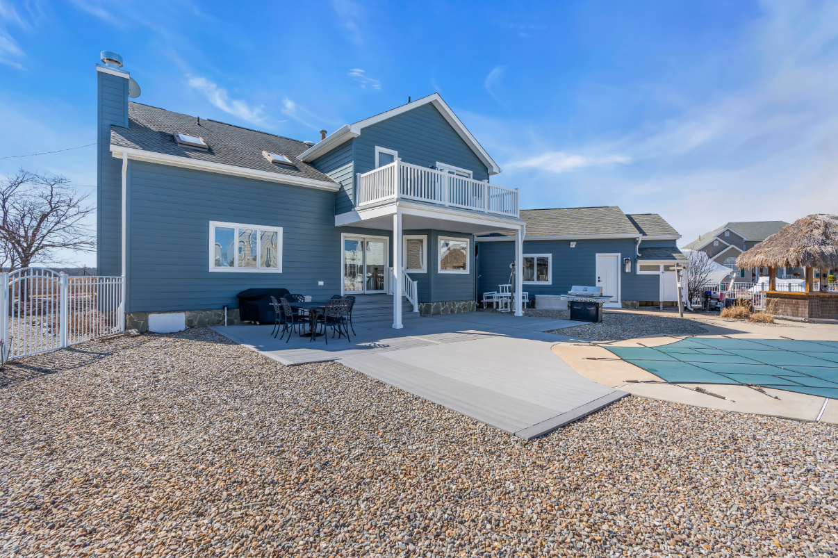 Backyard of Bayville NJ home with elevated deck, outdoor furniture, and a pebbled landscape surrounding a covered in-ground pool.