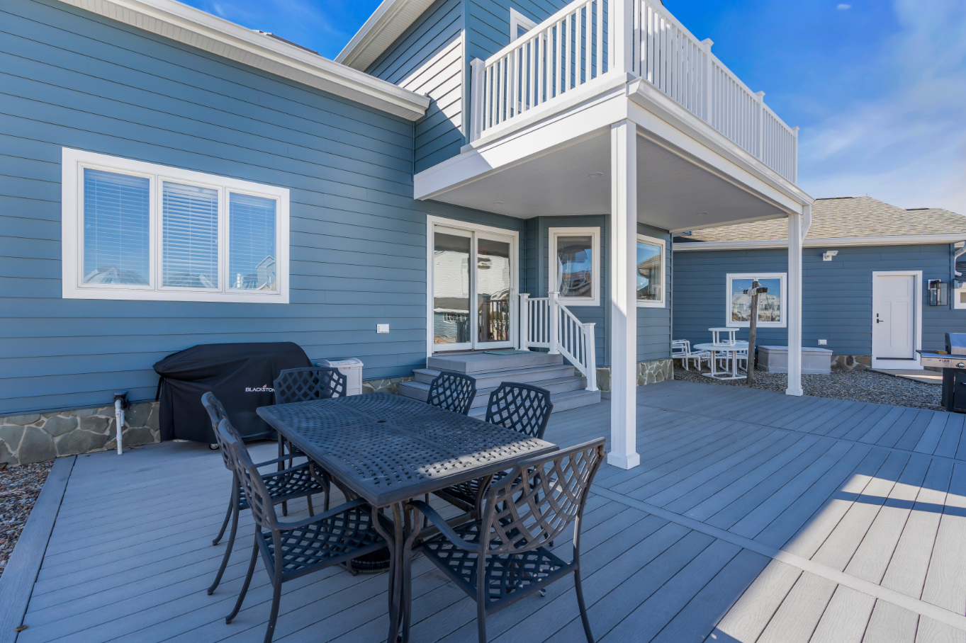 Close-up of rear deck area with metal dining table and chairs, white railing, and sliding doors leading into the home Bayville NJ.