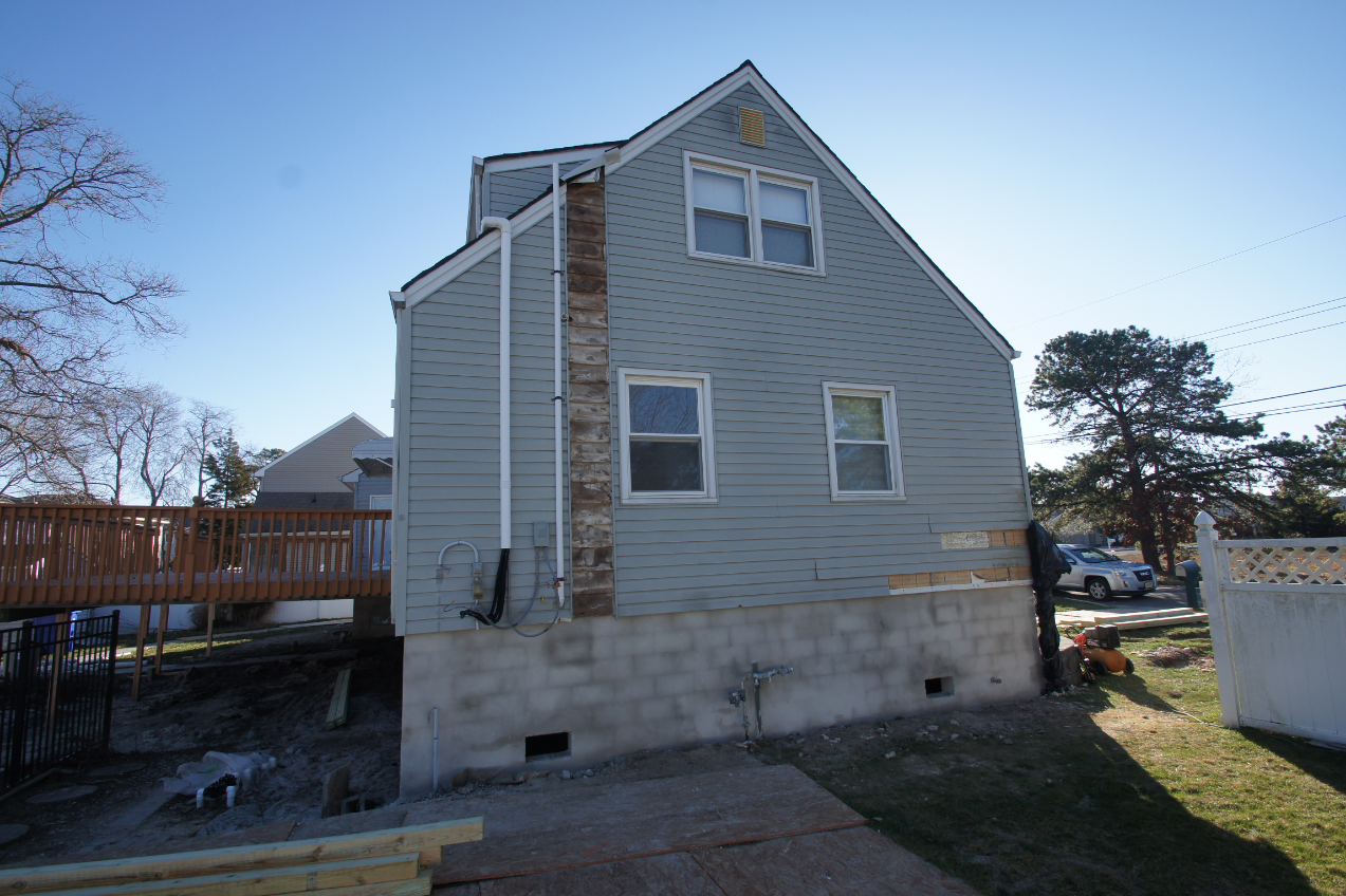 Side view of new concrete block foundation and visible utility adjustments during house lifting and foundation replacement in Toms River NJ