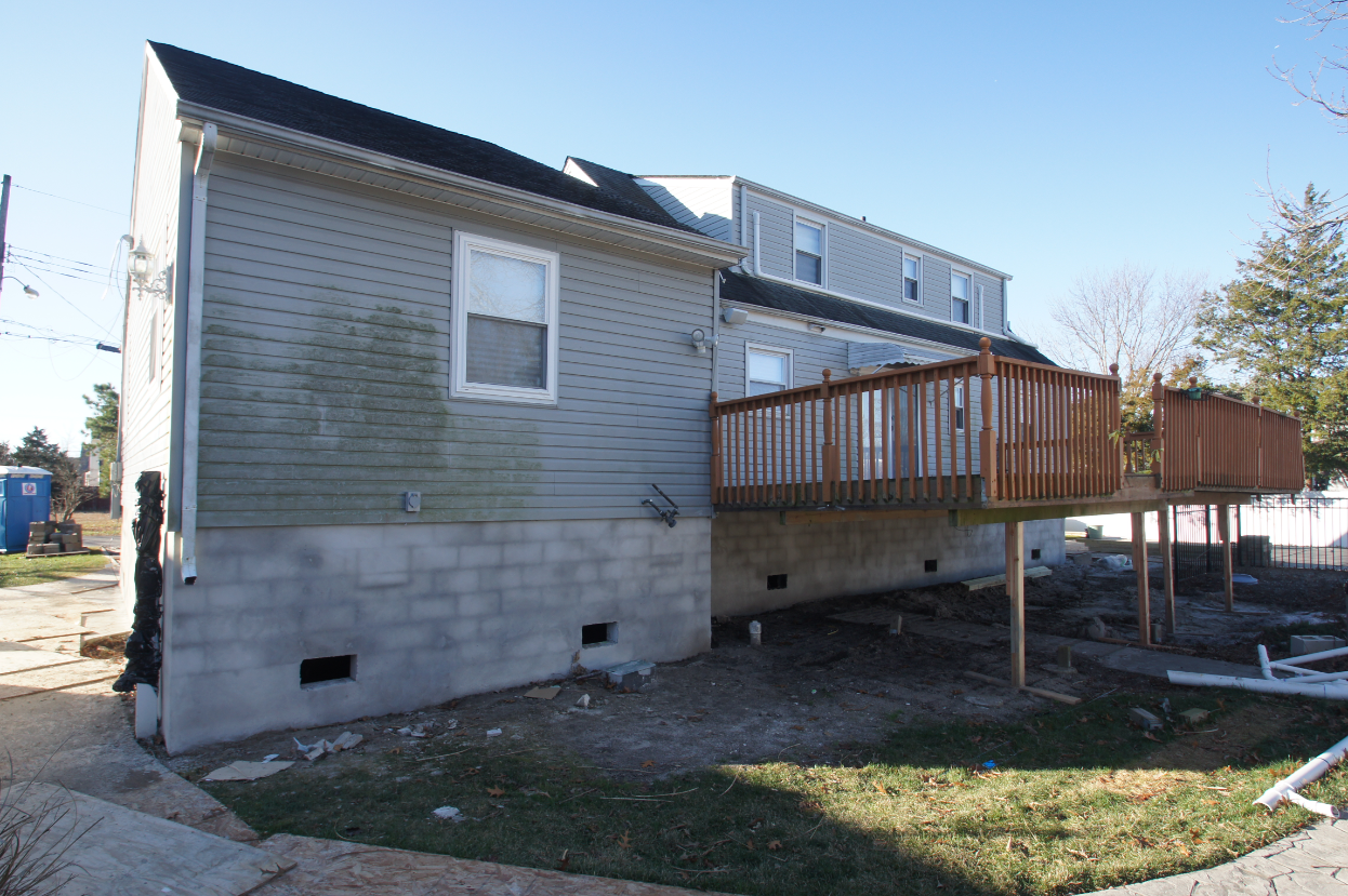 Side view of elevated house in Toms River NJ showing new concrete block foundation and raised wooden rear deck, part of full home elevation project.