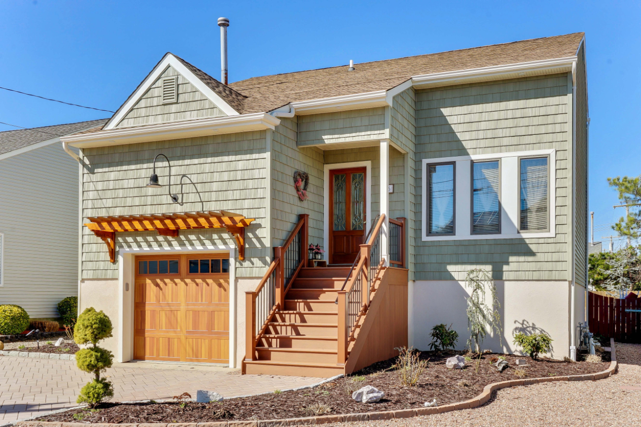 Front angle of house lift and exterior renovation in Toms River, NJ, featuring new green shake siding, custom cedar garage door, and composite front stairs.