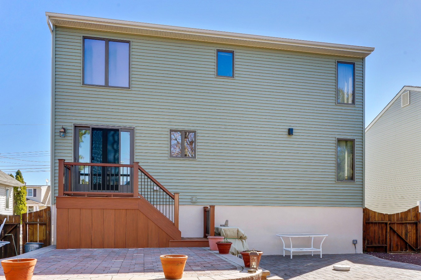Rear view of home lift in Toms River, NJ, displaying newly installed vinyl siding, backyard patio, and second-entry stairs.