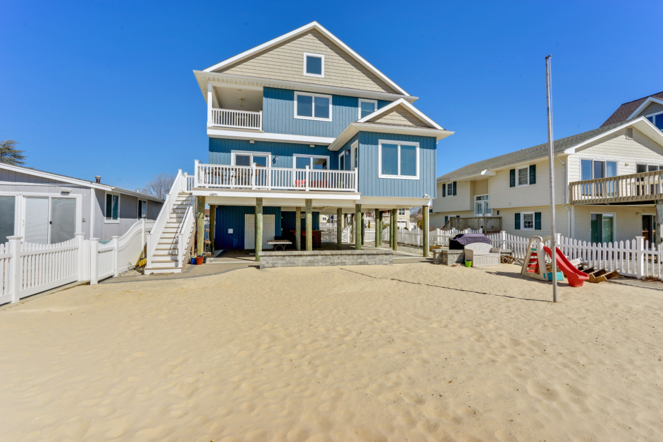 Rear facade of beachfront home with raised deck, outdoor stairs, and direct beach access