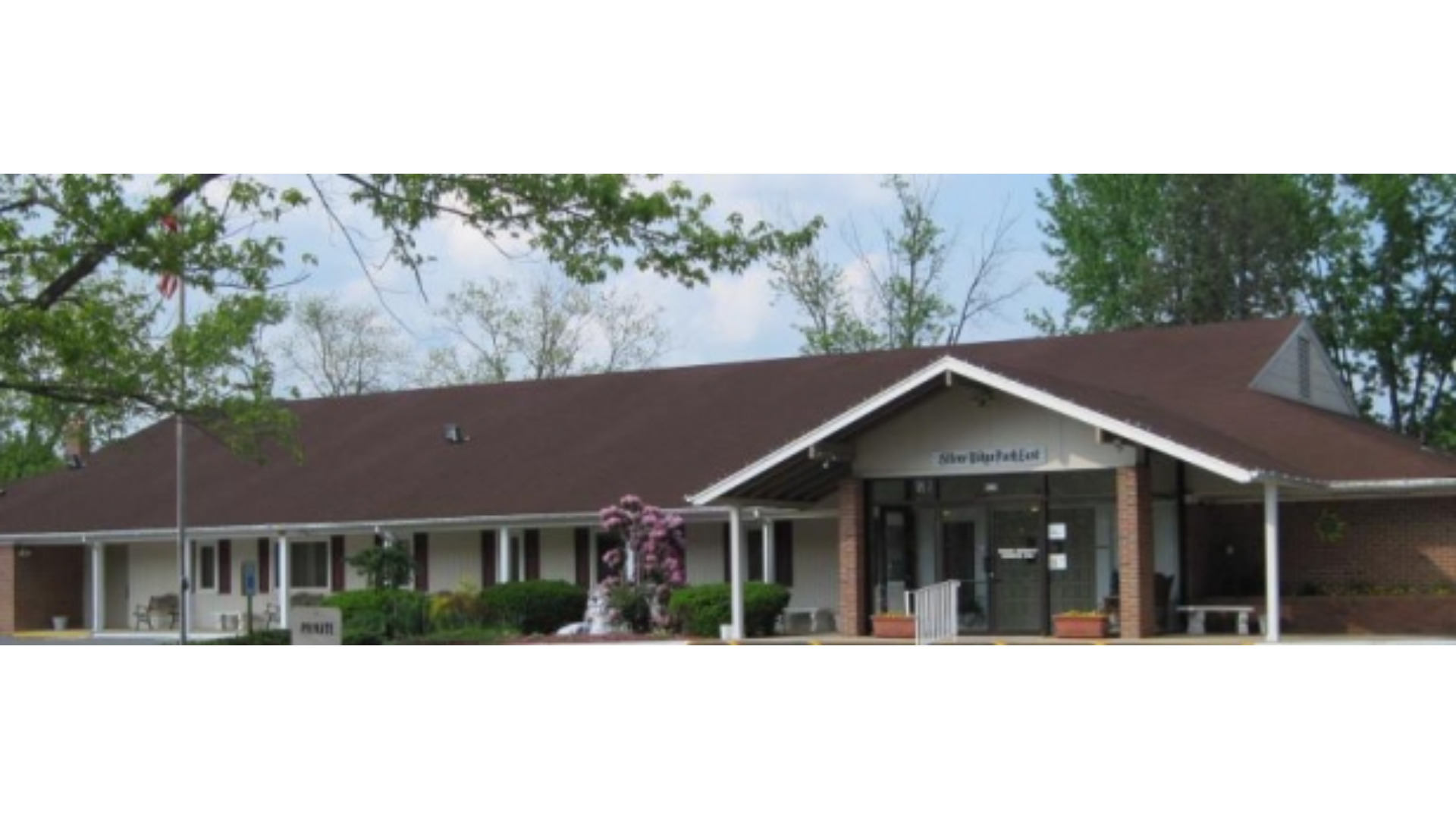 Front entrance of the Silver Ridge Park East community center in Toms River, New Jersey, featuring a brown roof, white pillars, landscaped greenery, and glass double doors under a gabled roof. J.A.Y. Construction