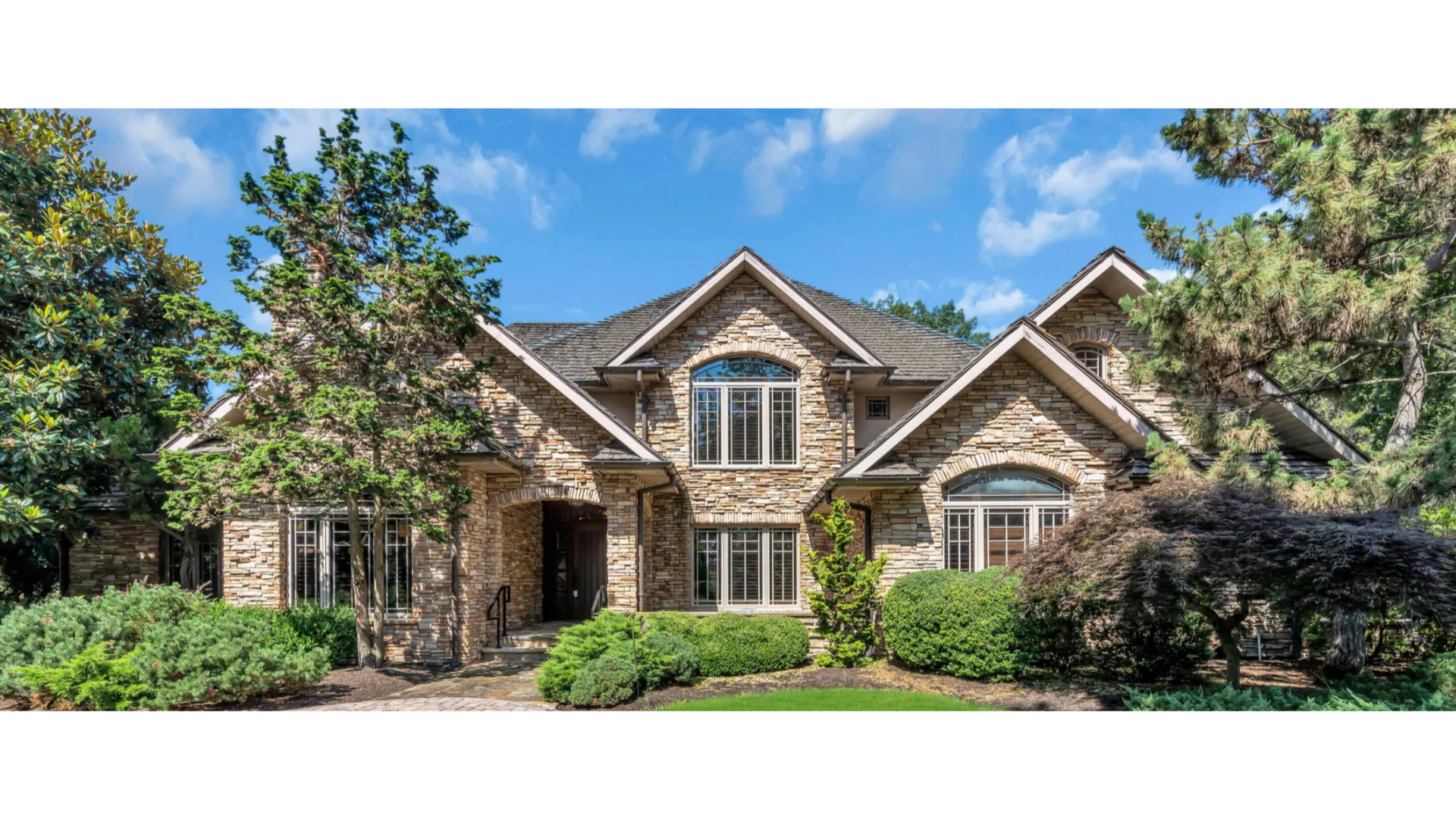 Stately stone-front home in Wall Township, NJ with architectural roofing and lush landscaping. J.A.Y. Construction is the premier local contractor for roofing, siding, and exterior renovations in Monmouth County.
