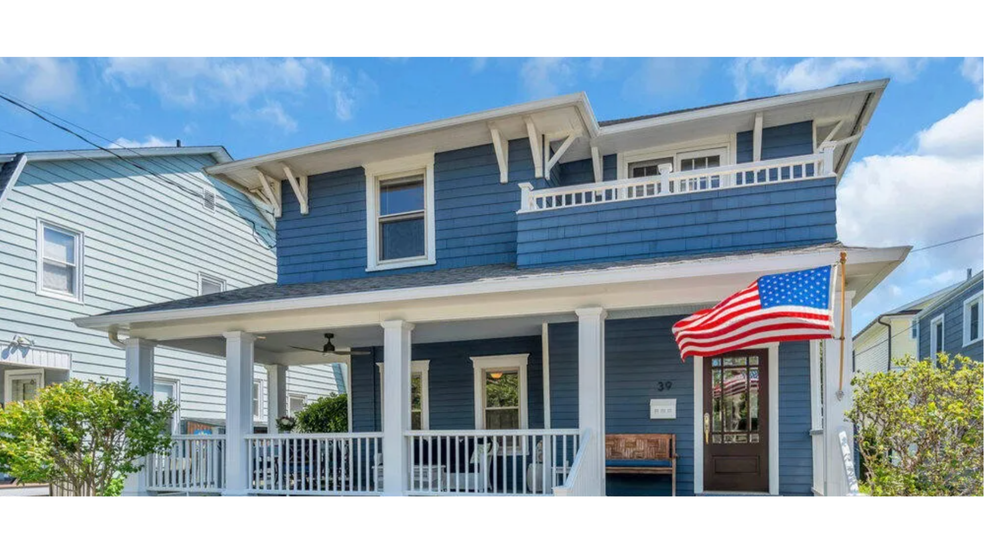 Classic blue coastal home in Avon-by-the-Sea, NJ with a wide front porch, American flag, and shingle siding. J.A.Y. Construction is a trusted local expert for roofing and siding along the Jersey Shore.