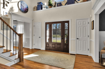 Grand two-story entryway renovation by J.A.Y. Construction with hardwood floors, staircase with black iron balusters, double front doors, and natural light.