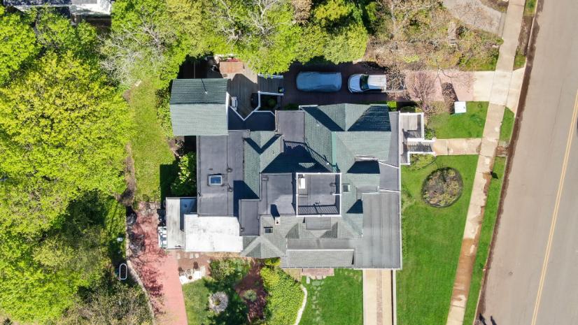 Drone view of a multi-level residential roof with gables, dormers, and skylights on a landscaped suburban New Jersey home. 