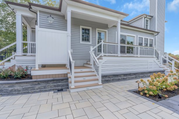 Covered porch and deck renovation by J.A.Y. Construction with composite steps, white railing, privacy panels, vinyl siding, and custom exterior lighting.