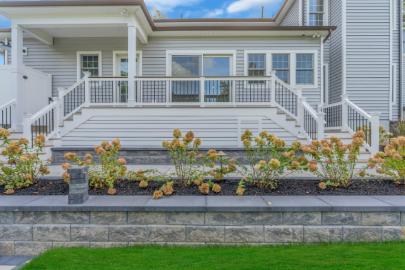 Rear porch renovation by J.A.Y. Construction showcasing composite decking, black cable rail system, vinyl siding, and landscaped retaining wall.