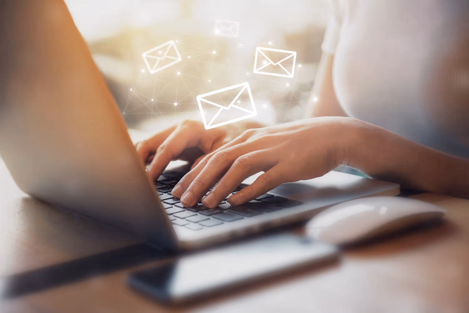 Closeup of woman's hands using a laptop with email icons as she types up a response.