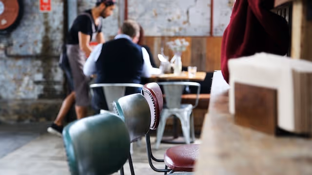 Empty chairs in a restaurant with a waiter serving tables in the background