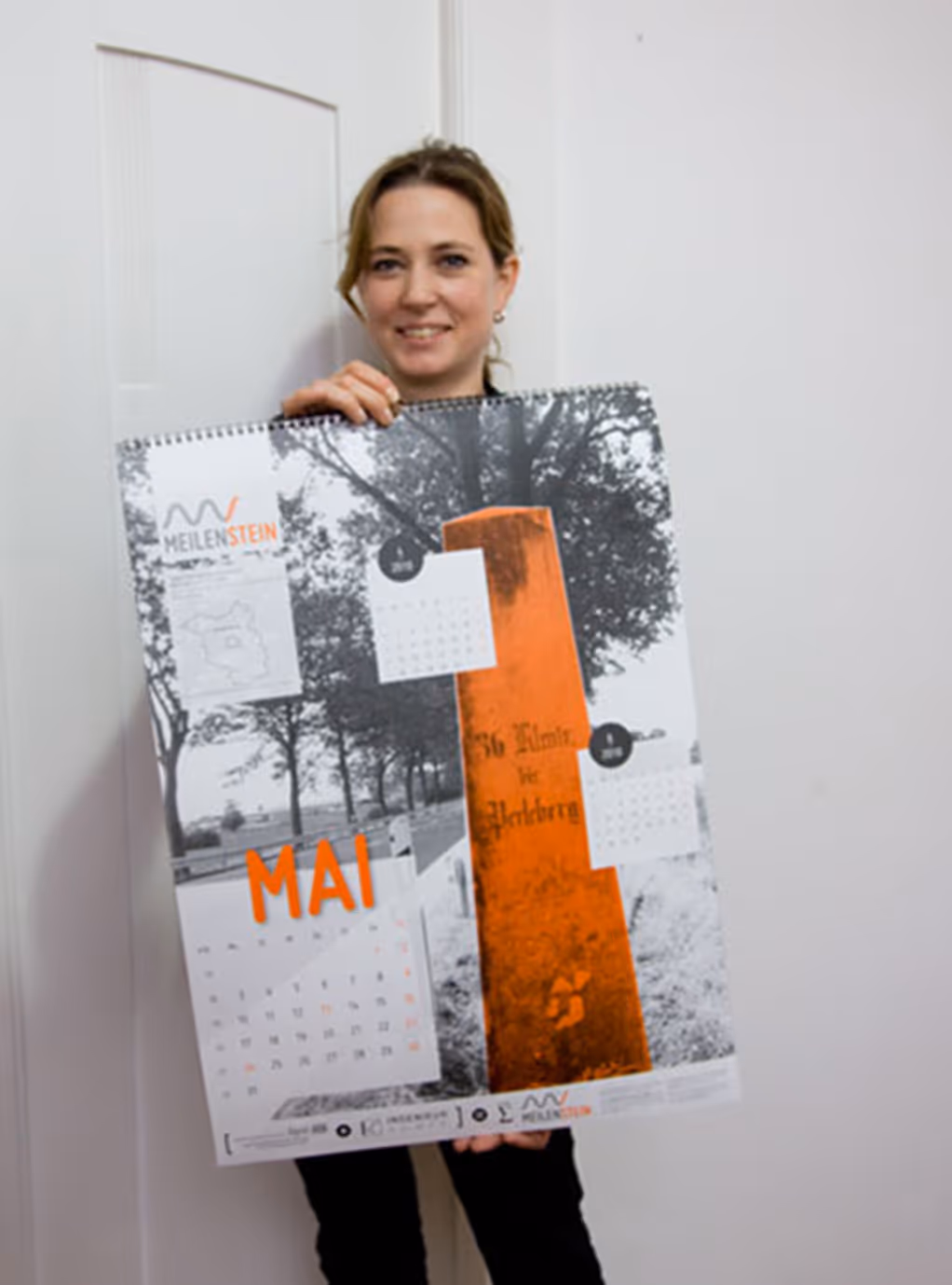 Astrid Paul hält eine großen Wandkalender für das Ingenieurbüro Meilenstein in der Hand
