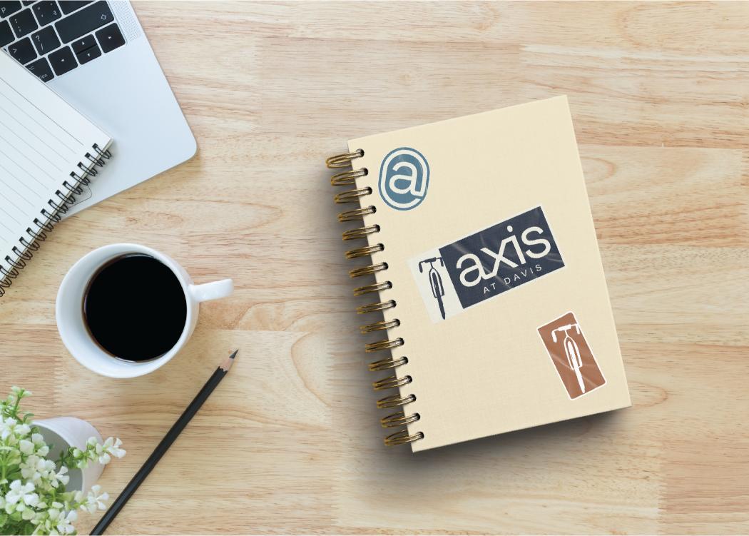 axis davis branded notebook with stickers placed on a table with a cup of coffee