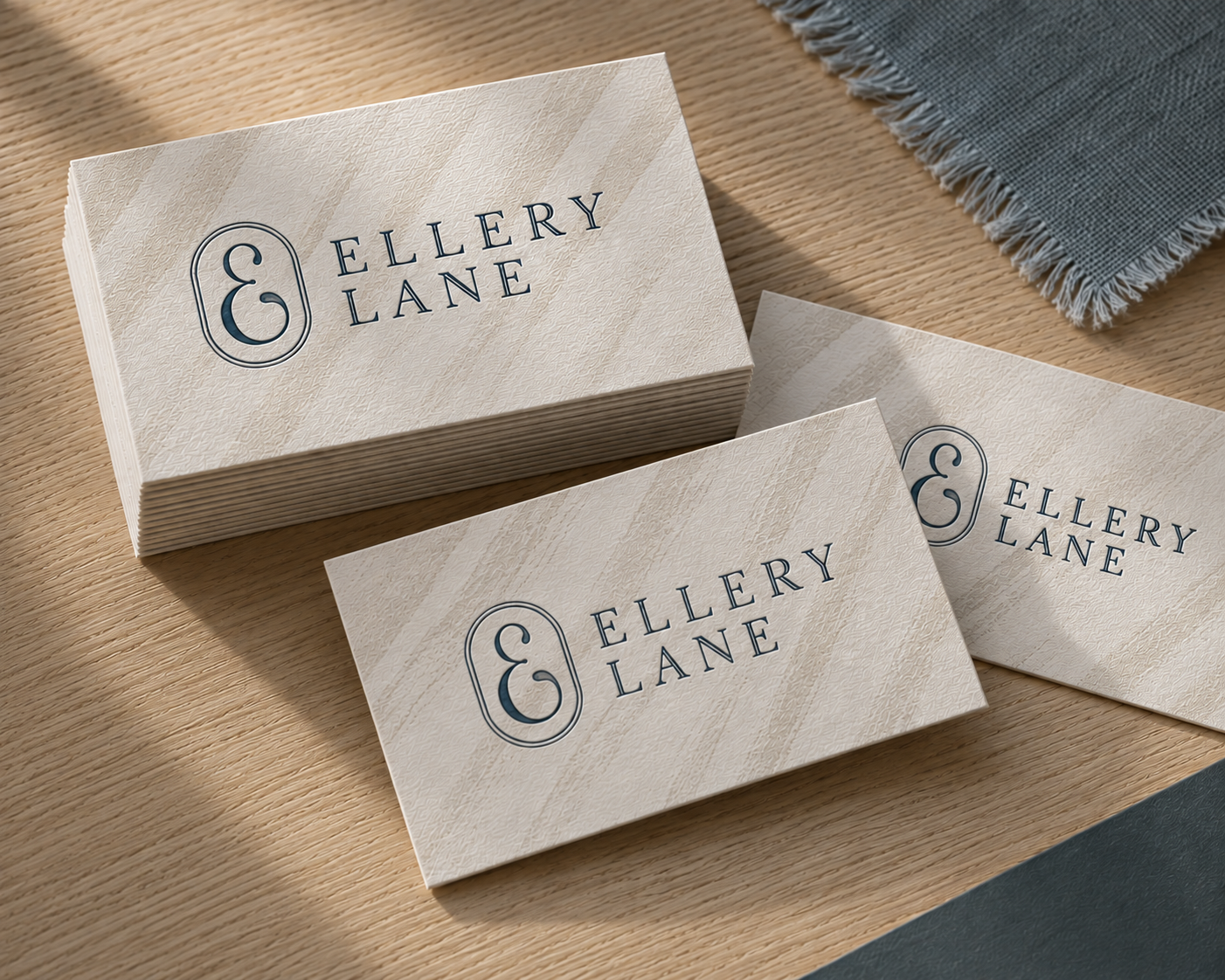 Ellery Lane business cards printed on textured Cotton paper with Harbor blue branding, arranged on a pale white oak surface with a soft blue-gray fabric accent.