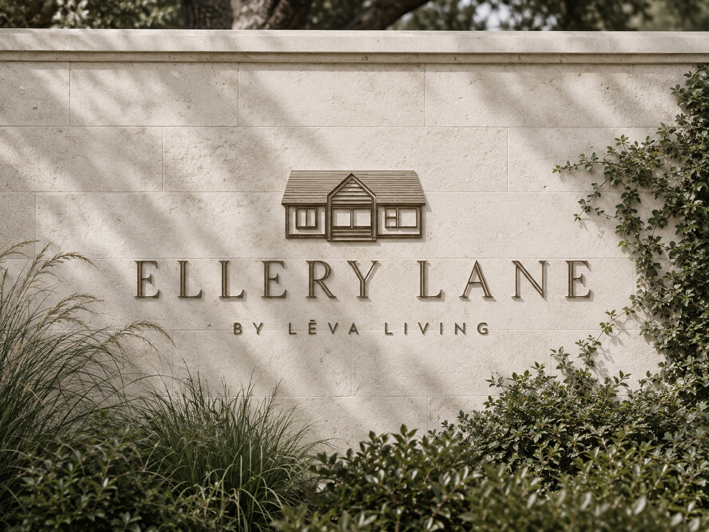 Ellery Lane monument sign with dimensional bronze lettering and cottage mark mounted on a light limestone wall, framed by lush landscaping and soft natural shadows.