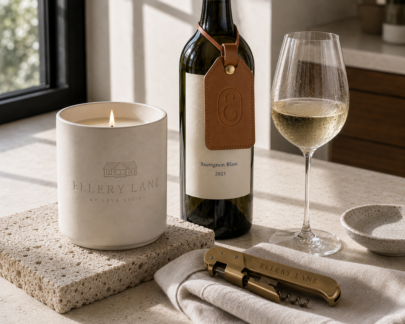 Ellery Lane wine and candle collection featuring a branded candle, Sauvignon Blanc bottle with embossed leather tag, white wine glass, and brass corkscrew styled in soft natural light.