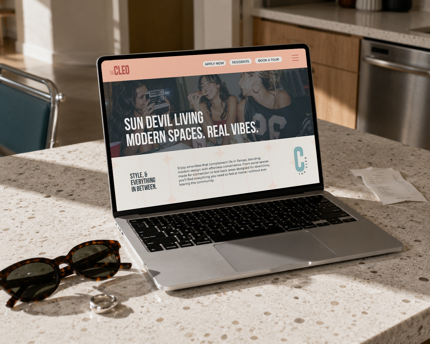 The Cleo Tempe website displayed on a laptop in a sunlit apartment kitchen, showcasing the brand’s playful visual identity and student-focused messaging.