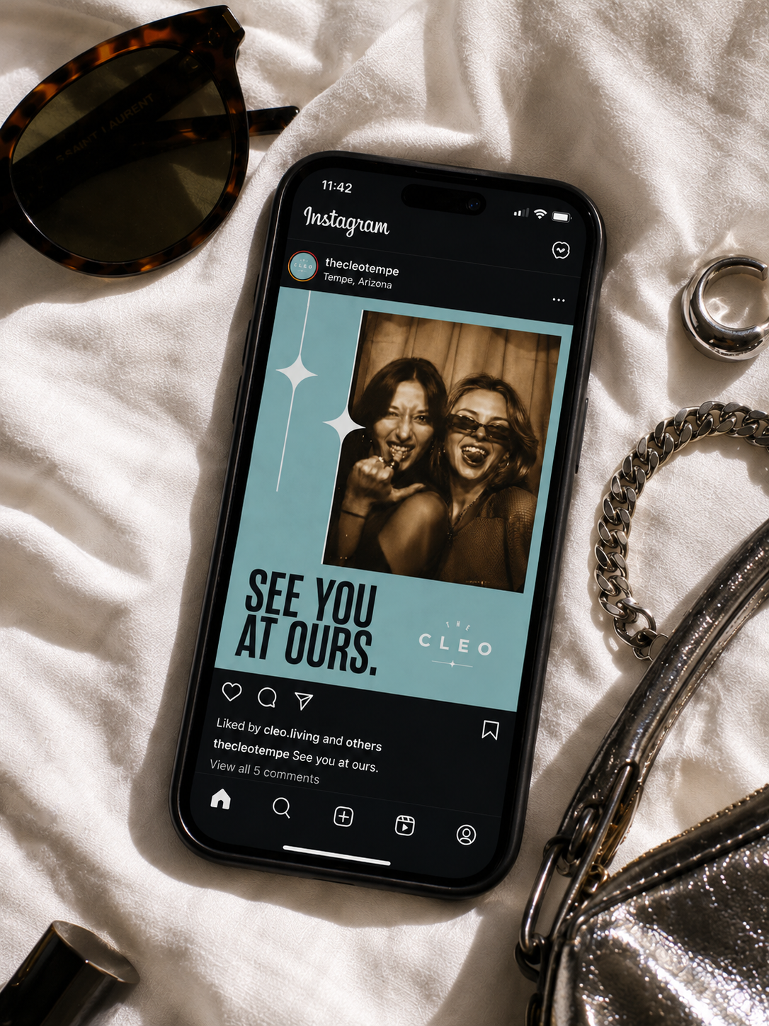 The Cleo Tempe Instagram post displayed on a smartphone, featuring a playful tour promotion surrounded by sunglasses and silver accessories.