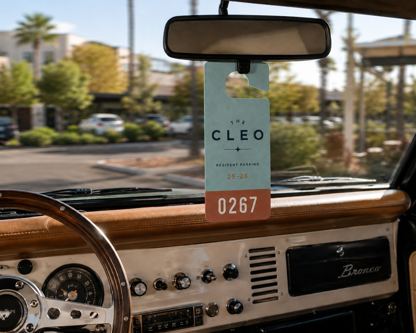The Cleo resident parking pass hanging from the rearview mirror of a vintage Ford Bronco, featuring teal and clay brand colors.