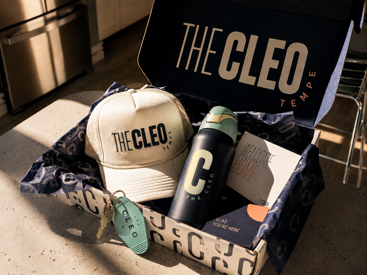 The Cleo Tempe welcome box filled with branded resident essentials, including a trucker hat, water bottle, key tag, and welcome materials.