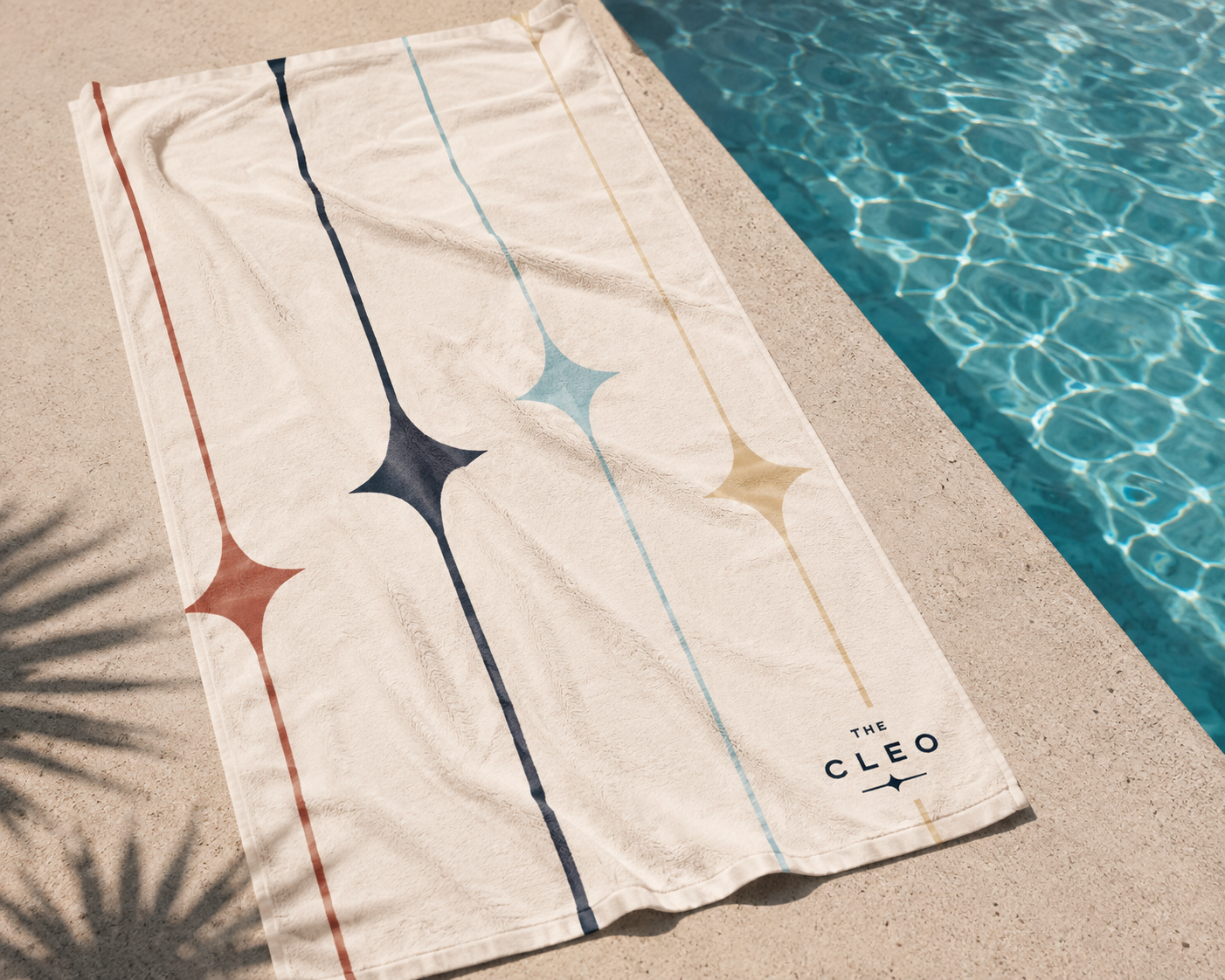 The Cleo branded pool towel featuring colorful starburst graphics and the logo, laid beside a sunlit swimming pool.