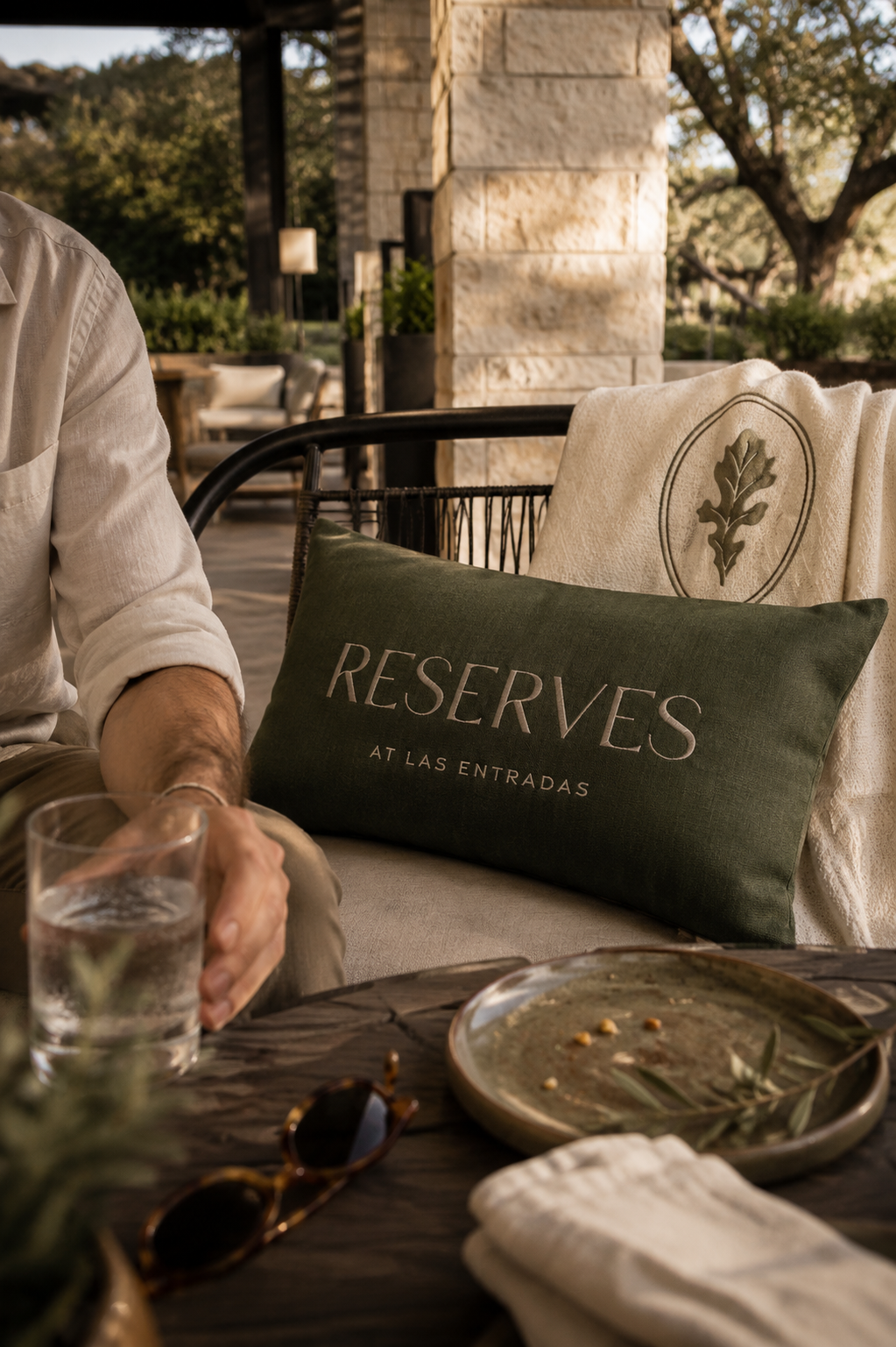 Reserves at Las Entradas branded pillow and oak leaf throw styled in an outdoor lounge, with warm natural light and relaxed residential details.