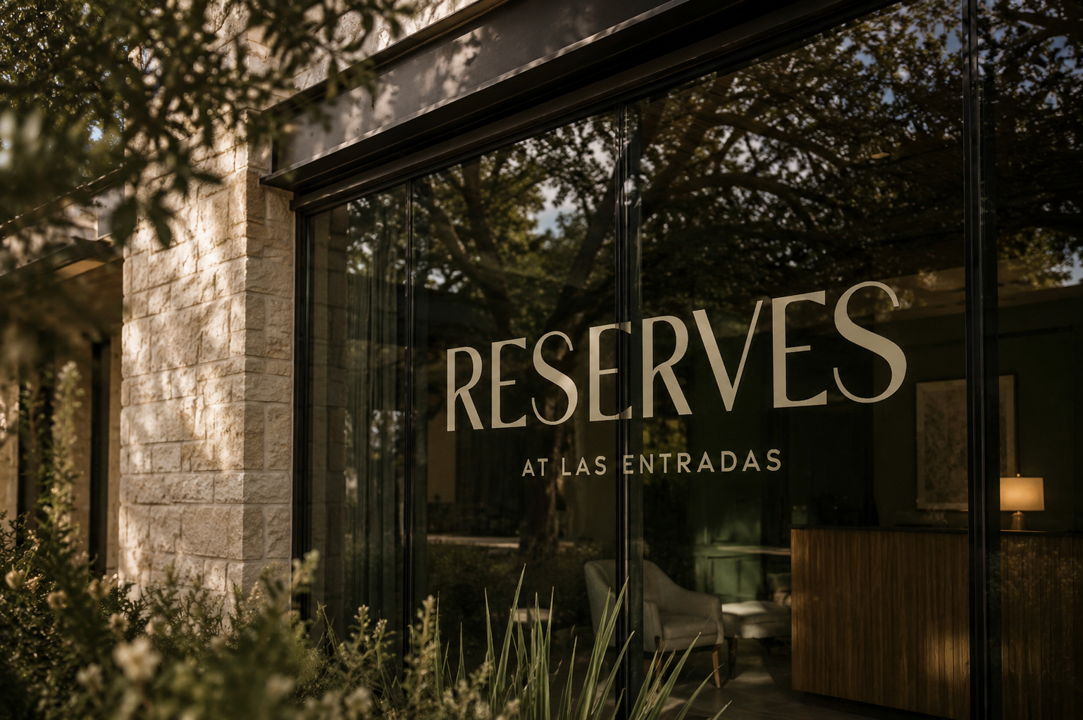 Reserves at Las Entradas logo applied to floor-to-ceiling glass windows framed by limestone architecture and native landscaping.