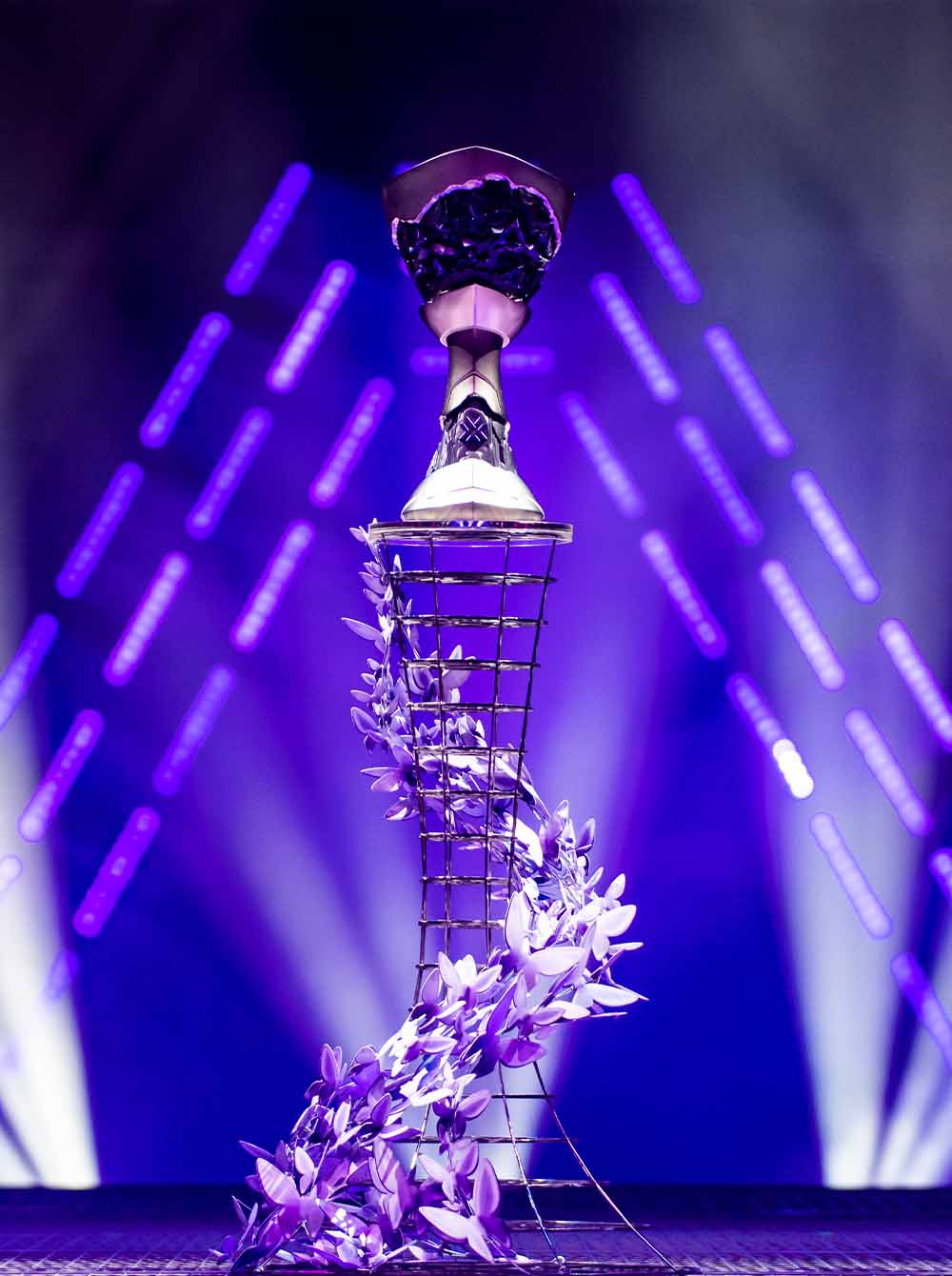 Decorative trophy with ascending metal frame and purple floral arrangement under purple lights.