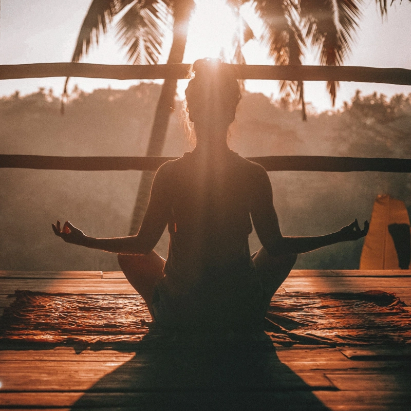 Person meditating on a deck at sunset
