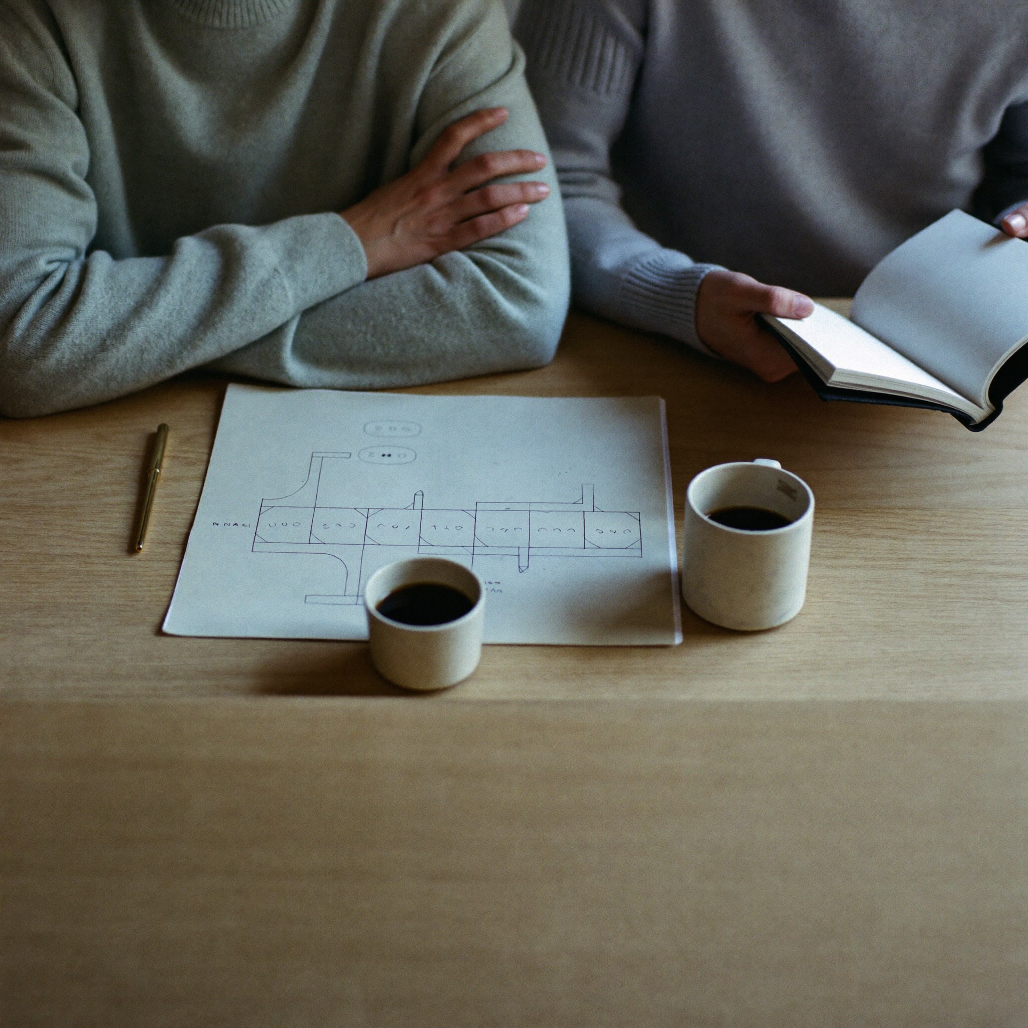 Two people meeting over coffee with a hand-drawn process sketch on the table