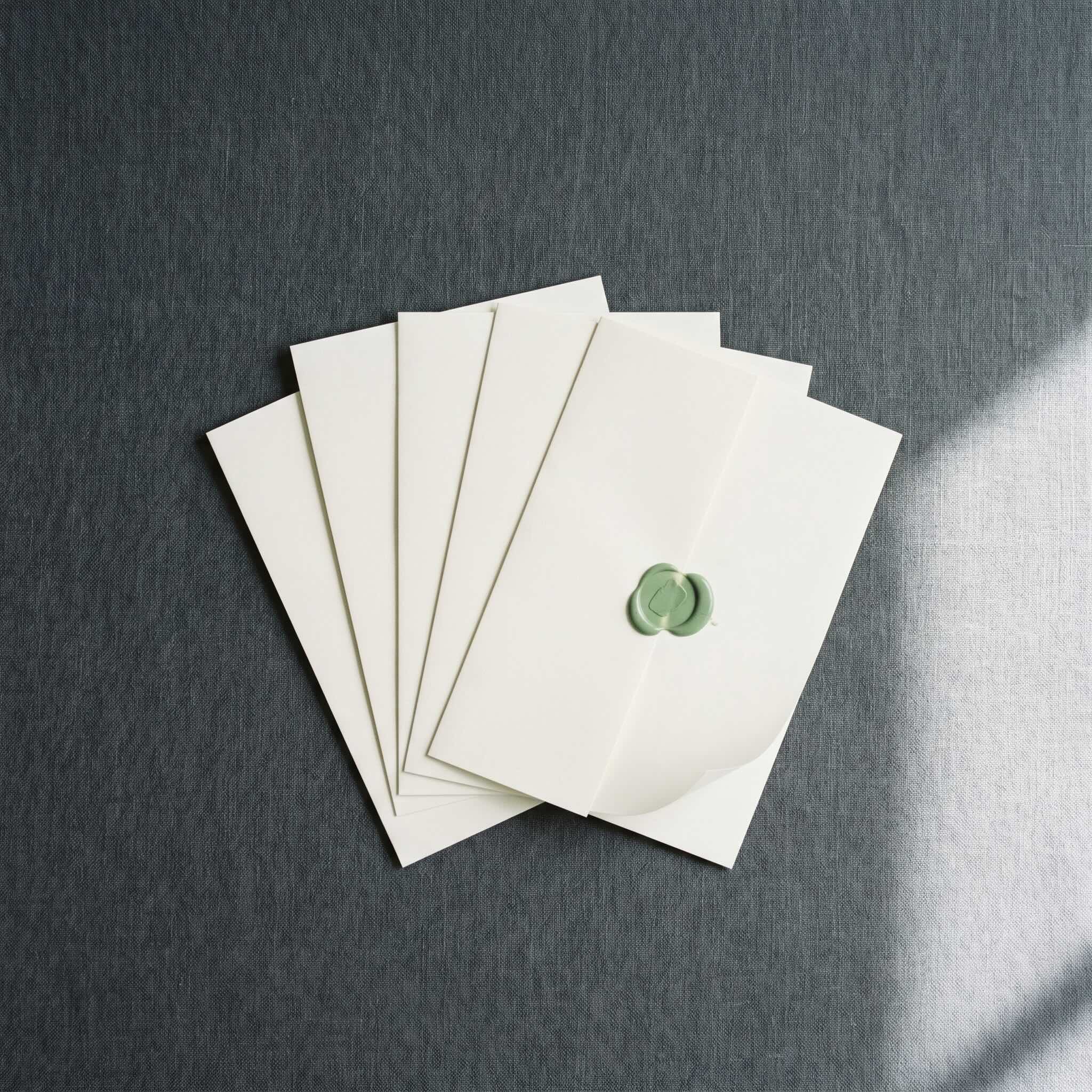 Five ivory envelopes stacked, the top one sealed with a green wax seal