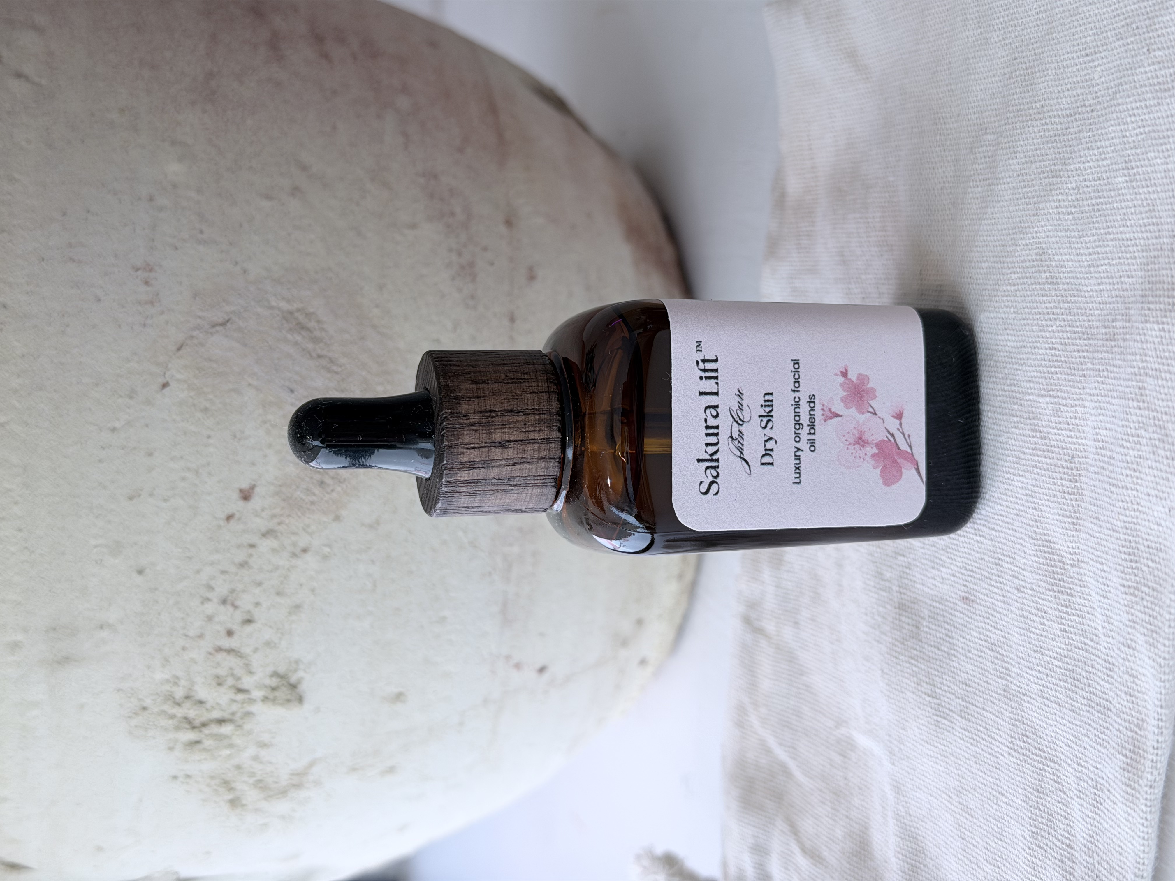 Bottle of Cherry Blossom facial massage oil on marble table with a woman applying oil to her face.