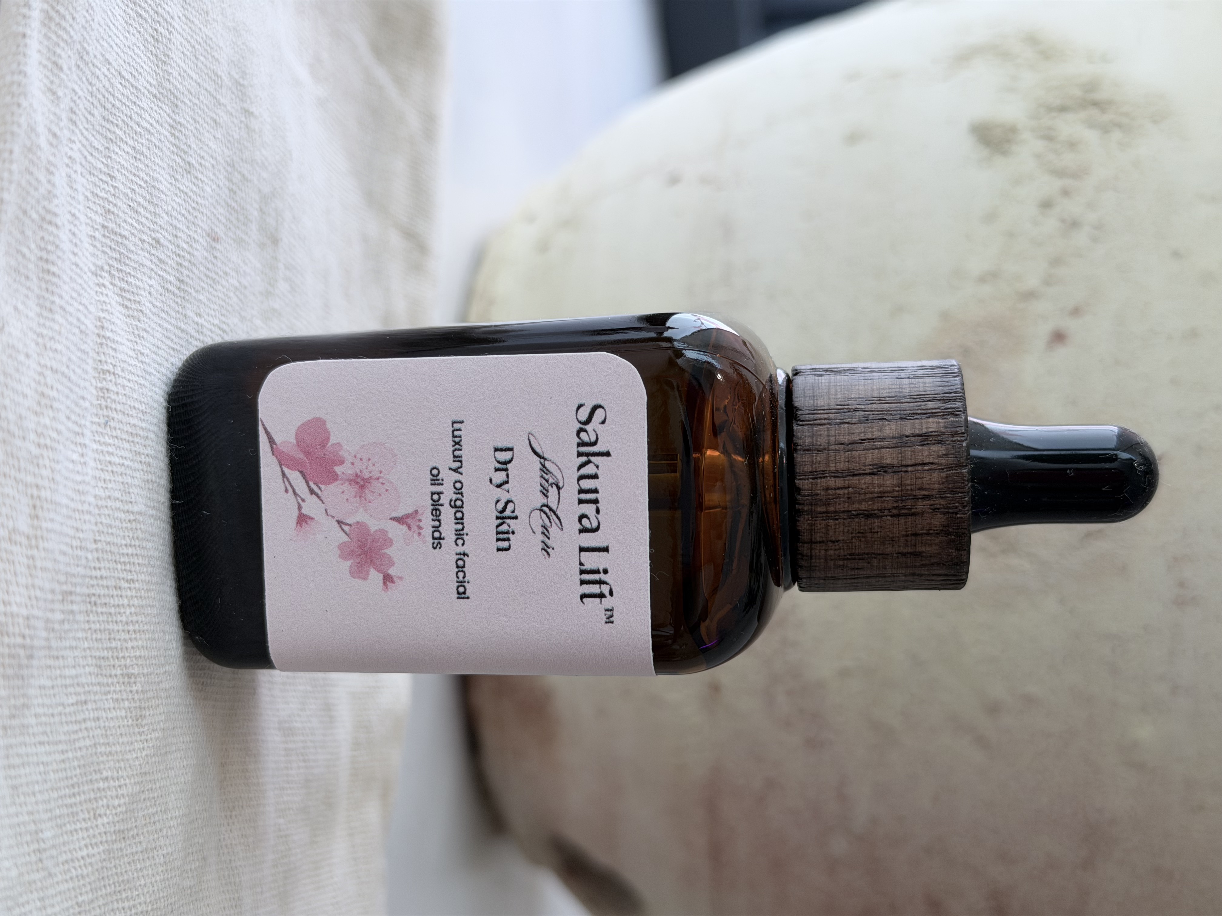 Bottle of cherry blossom facial massage oil with wooden dropper on marble surface with flowers.