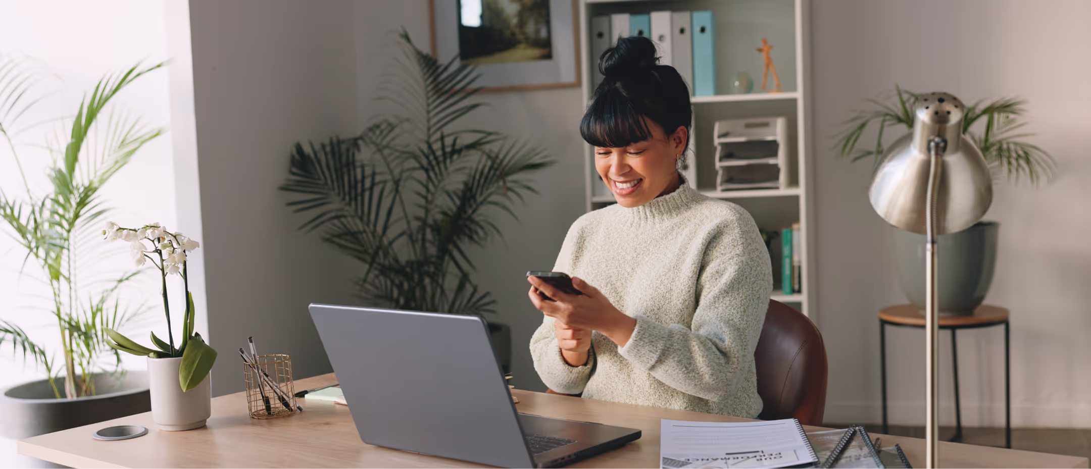 woman sitting on desk in home holding her phone to contact