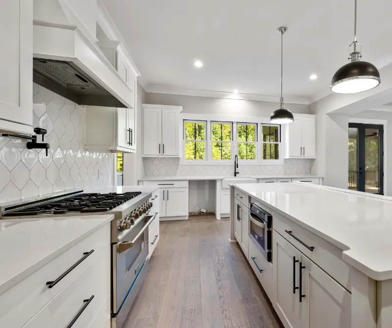 Modern kitchen with white cabinetry, large island, stainless steel gas stove, and pendant lights.
