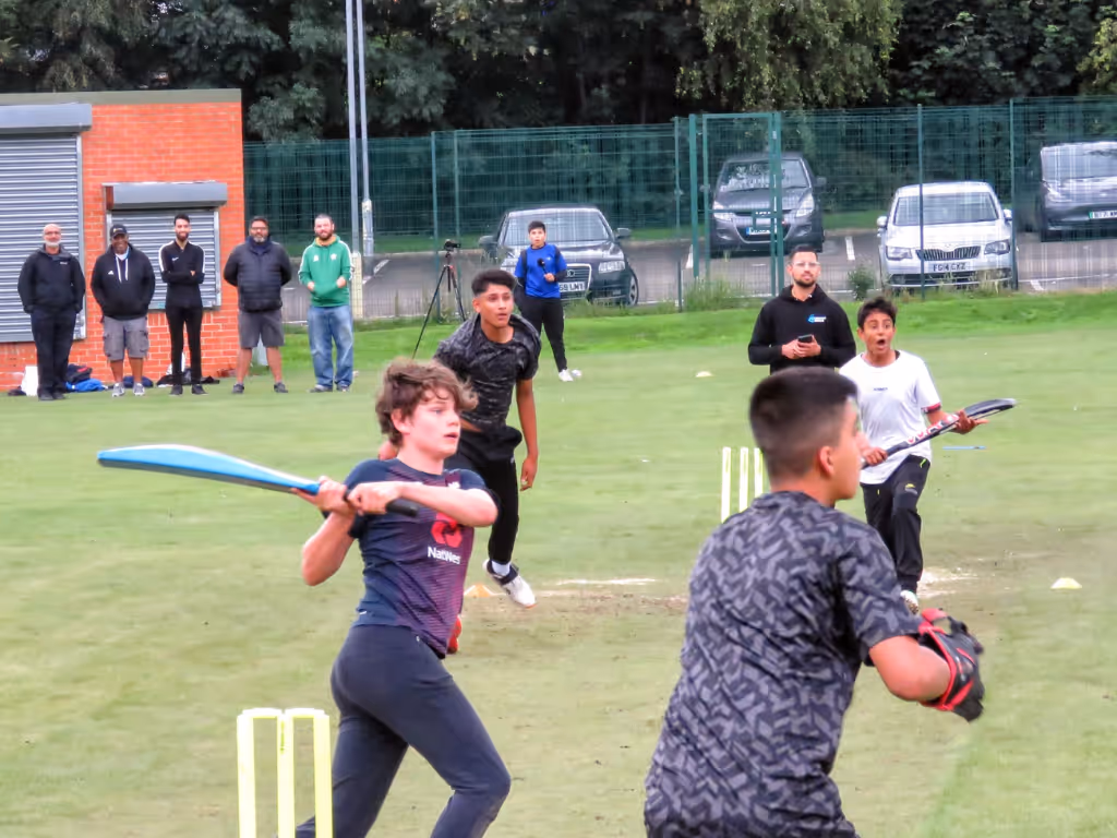 Junior batter playing a creative switch hit during Cricket Arena’s Junior Hundred tournament at Shiregreen Cricket Club in Sheffield, as the bowler and wicketkeeper watch on in a competitive under-15s match showcasing high skill and confidence.