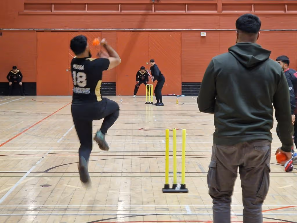 Bowler captured mid-air in bowling action as the batsman prepares to face the ball during an indoor Cricket Arena Mini Bash League match at Concord Sports Centre in Sheffield.