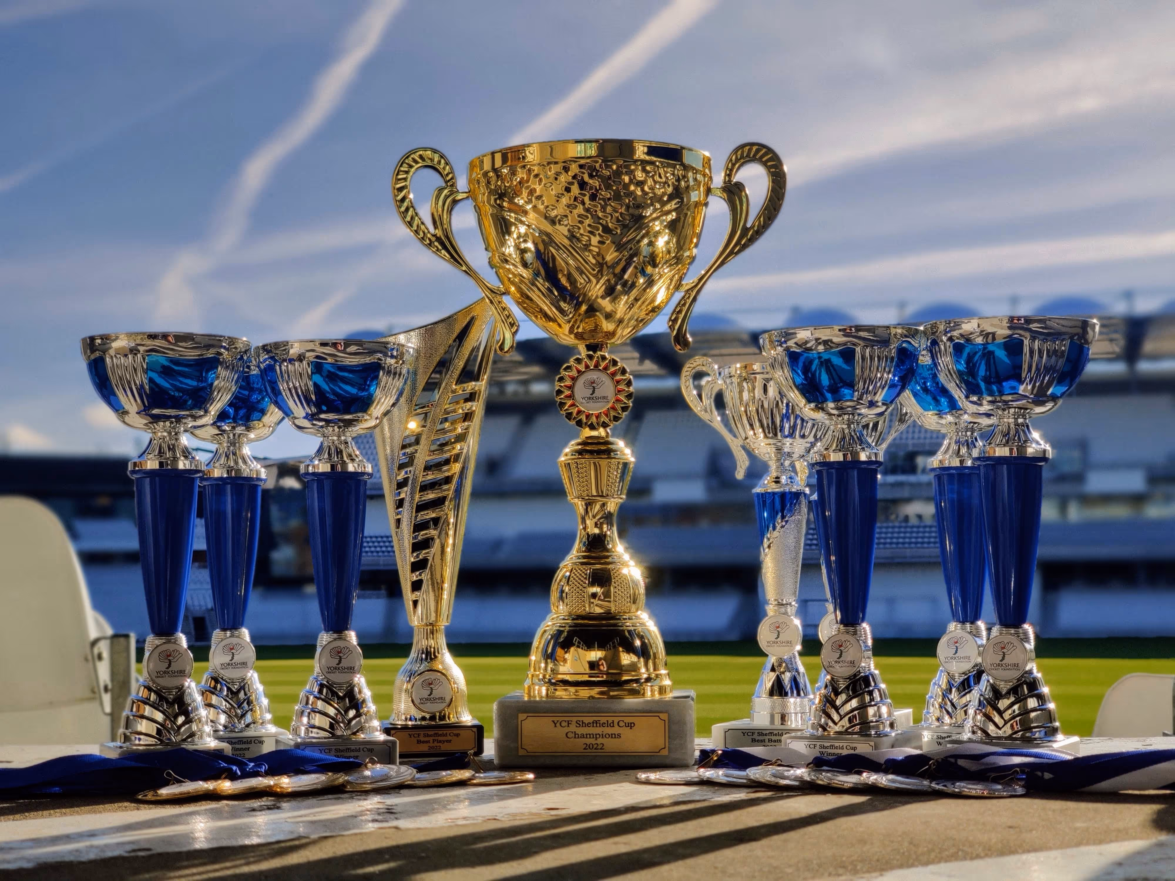 The YCF Sheffield Cup 2022 trophies — the grand champions’ cup and individual awards — displayed with the Yorkshire Cricket Foundation logo, set against the iconic Headingley Cricket Ground backdrop.
