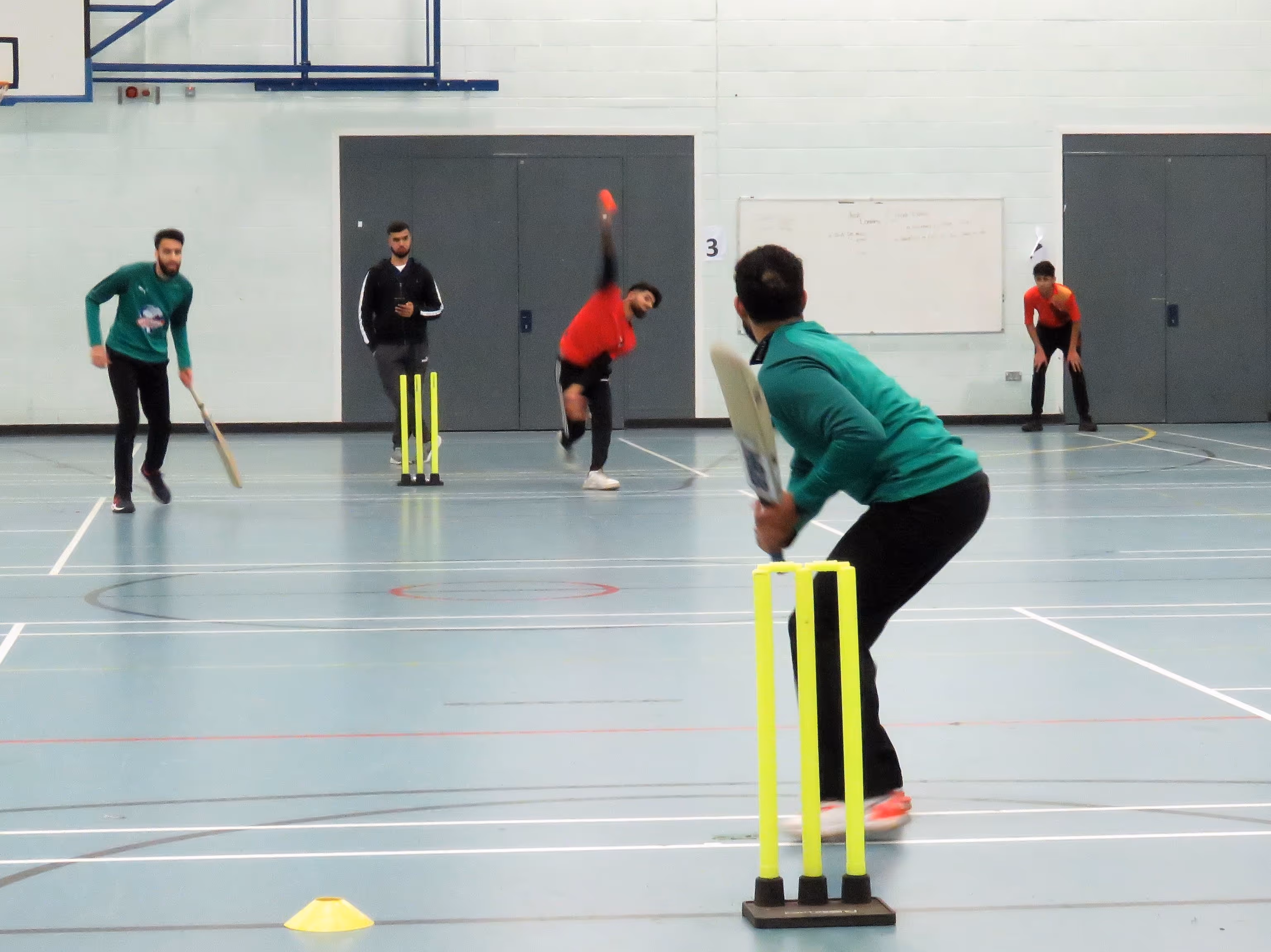 Action photo from Sheffield Cup 2022 at Sheffield Park Academy — a bowler charges in to deliver a windball to batter Adil Ibrahim, capturing the intensity and focus of indoor cricket play.