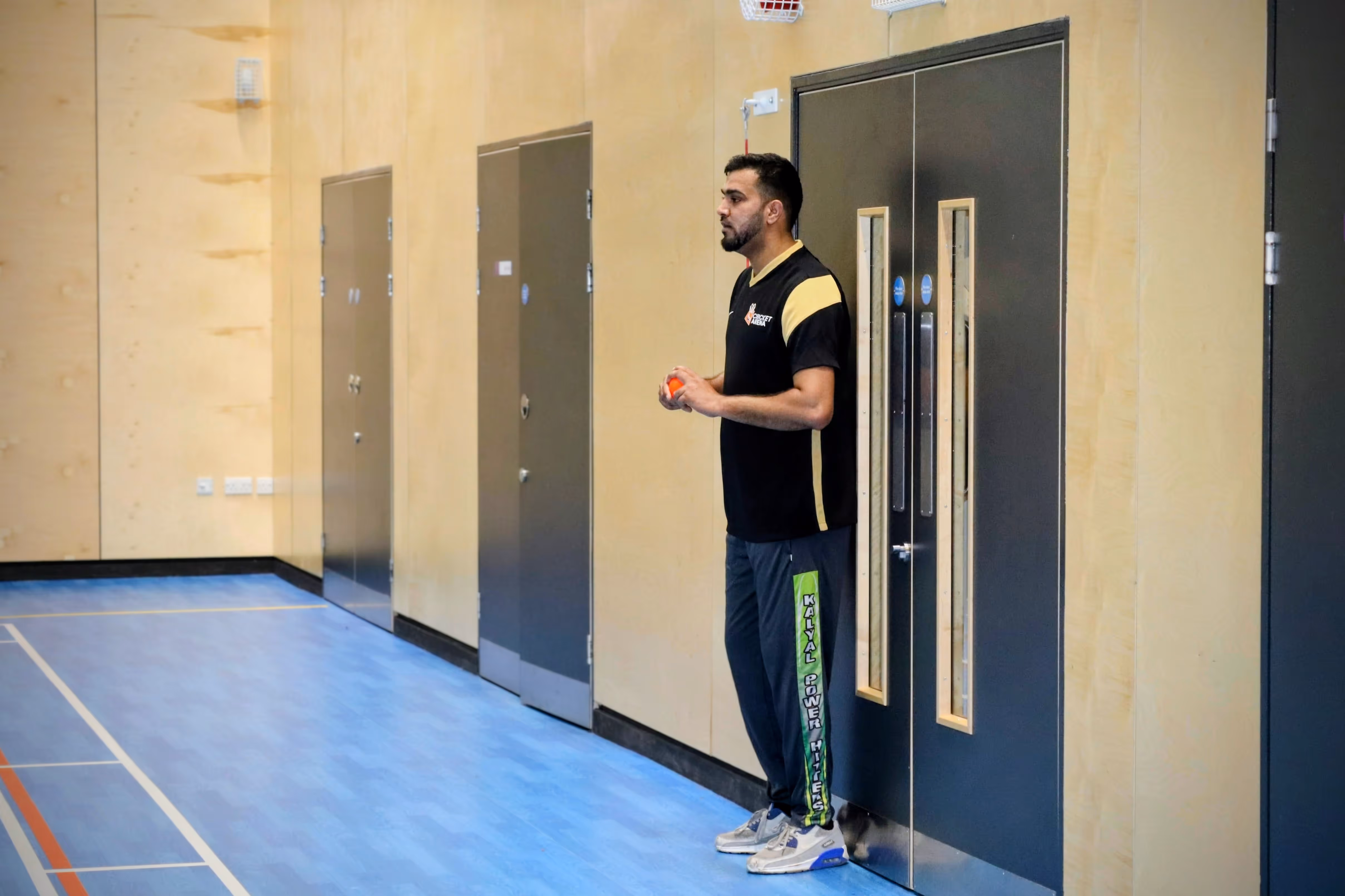 Danish Hussain stands focused at the end of his run-up, holding a windball in hand and preparing to bowl during the Yorkshire Indoor Finals, wearing his black and gold Cricket Arena kit.