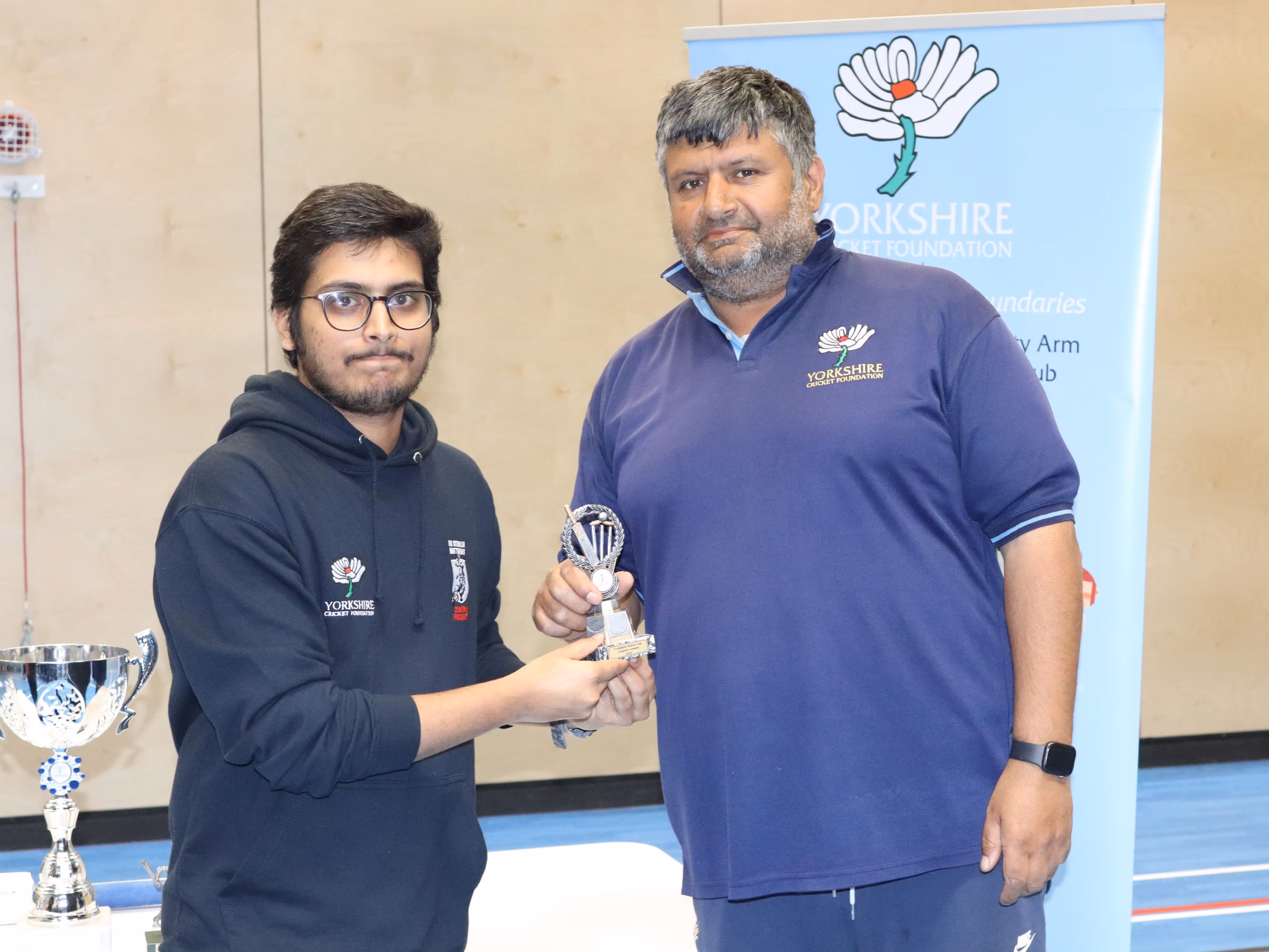 Yorkshire Cricket Foundation volunteer Akhil receiving an appreciation award for his umpiring and support, presented by Bradford Park Avenue head groundsman Nasa Hussain during the Yorkshire Indoor Finals ceremony.