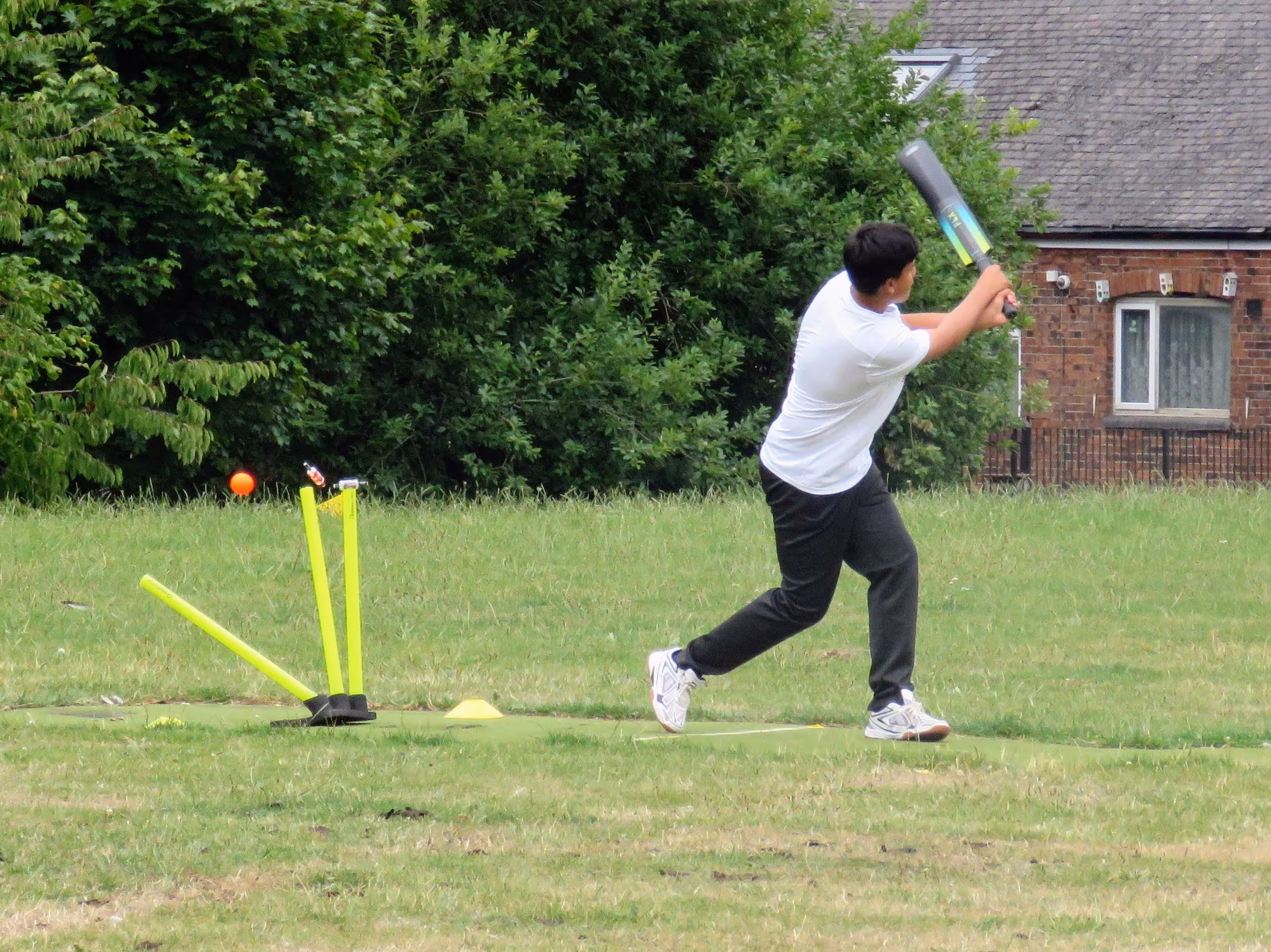 Action shot from the Junior Hundred 2022 showing a batter being bowled out on a non-turf wicket at Kashmir Gardens, with the orange windball flying past and the off stump cartwheeling after impact.
