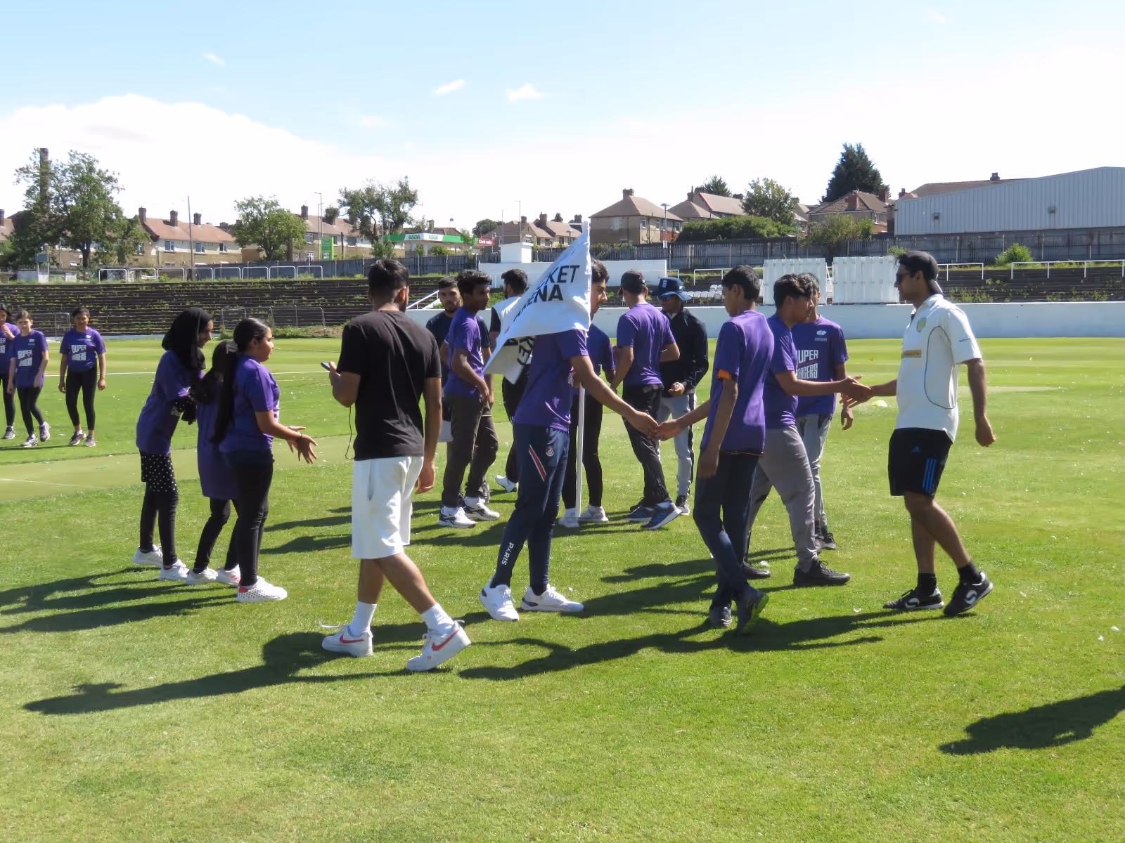 Players from both teams shake hands after the Junior Hundred 2022 final at Park Avenue, showing unity and respect. Sheffield players proudly hold the Cricket Arena flag.