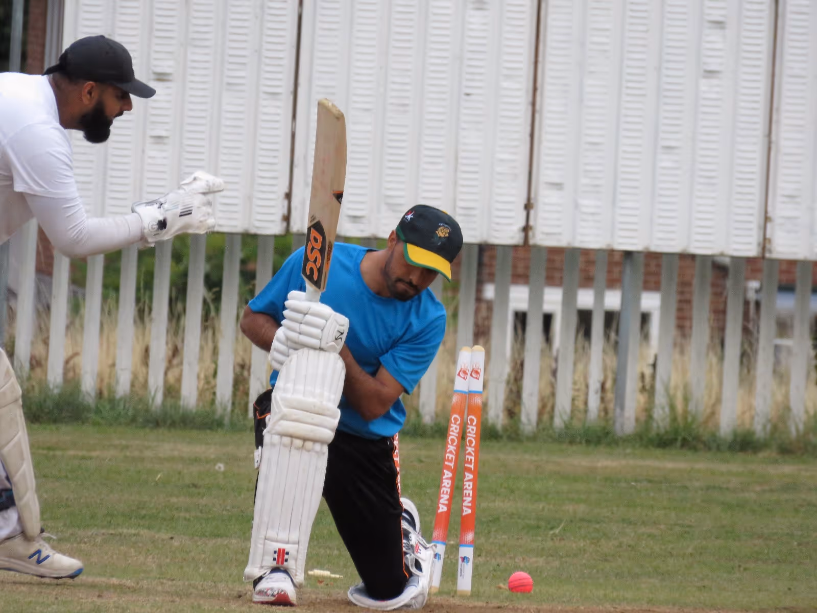 Light-hearted moment at Caribbean Sports Club as a batter looks down in disbelief after being bowled, while the wicketkeeper steps forward with playful banter in friendly spirit.